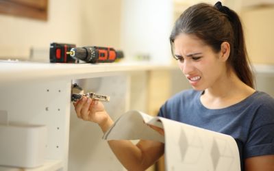 Junge Frau sitzt mit verzweifeltem Blick und einer Aufbauanleitung vor einem Küchenschrank