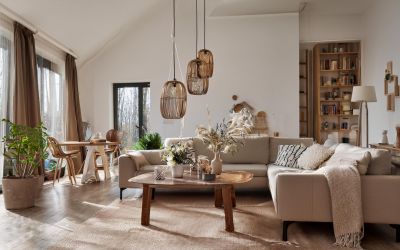 Hübsch dekoriertes Zimmer, mit beigem Sofa, braunen Vorhängen, Korblampen über dem Couchtisch aus Holz und kuscheligen Kissen.