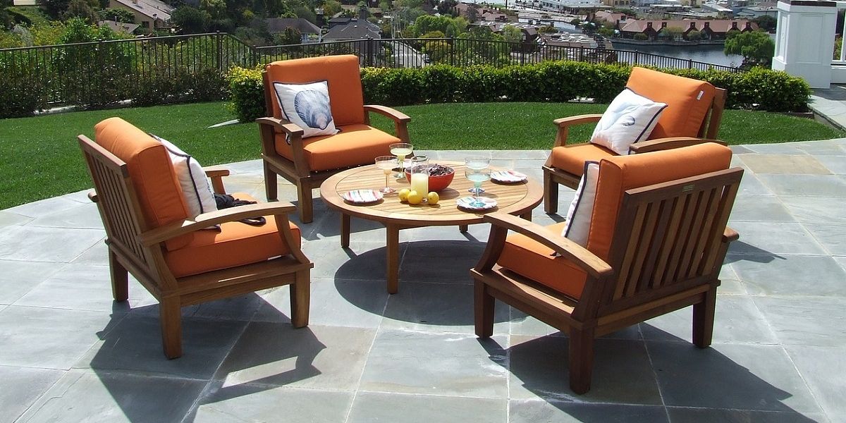 Vier gemütliche Teakholz-Sessel auf einer Terrasse, rund um einen gedeckten Teakholz-Tisch
