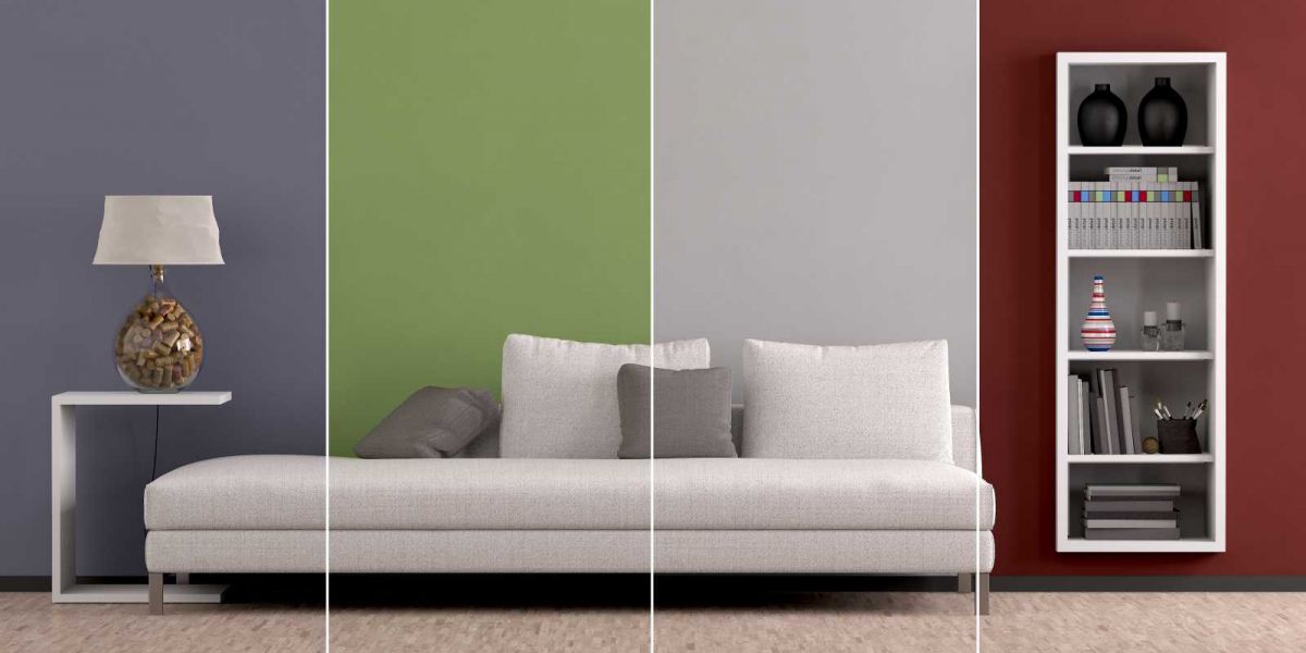 Wohnzimmerwand mit vier Farben gestrichen, davor ein beiges Sofa, ein kleiner Tisch und ein schmales Regal.